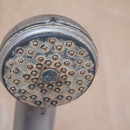 Clogged shower head with visible hard water stains and mineral buildup from untreated water