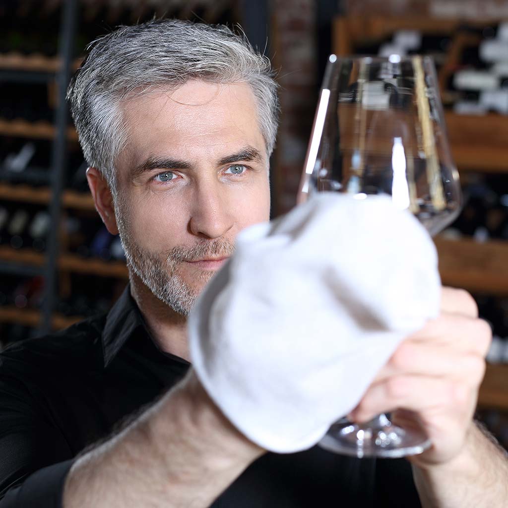 A handsome bartender polishes a glass of wine glasses.